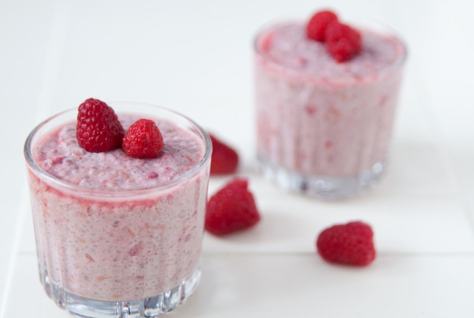 Two clear glasses holding pink chia pudding with raspberries on top.