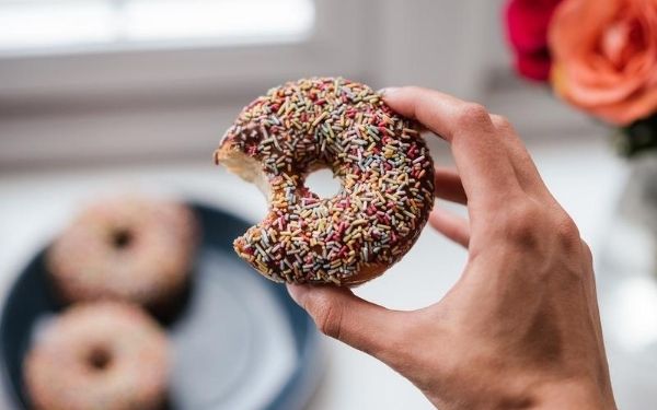 hand holding a chocolate donut with sprinkles that with a missing bite