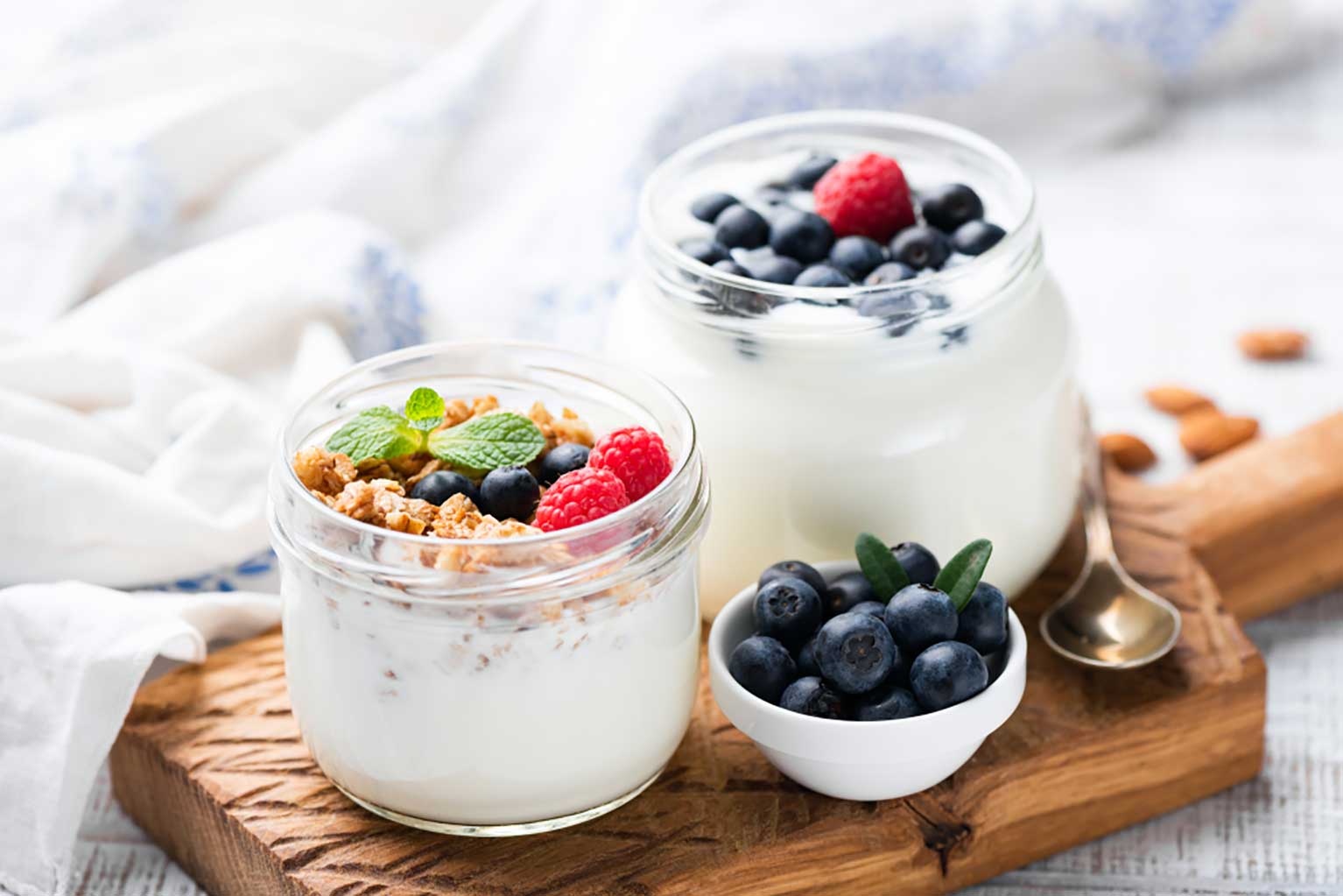 three glass bowls full of plain yogurt fruit and granola on a wooden board