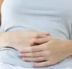 Siedząca kobieta trzymająca ręce na brzuchu - mdłości w ciąży