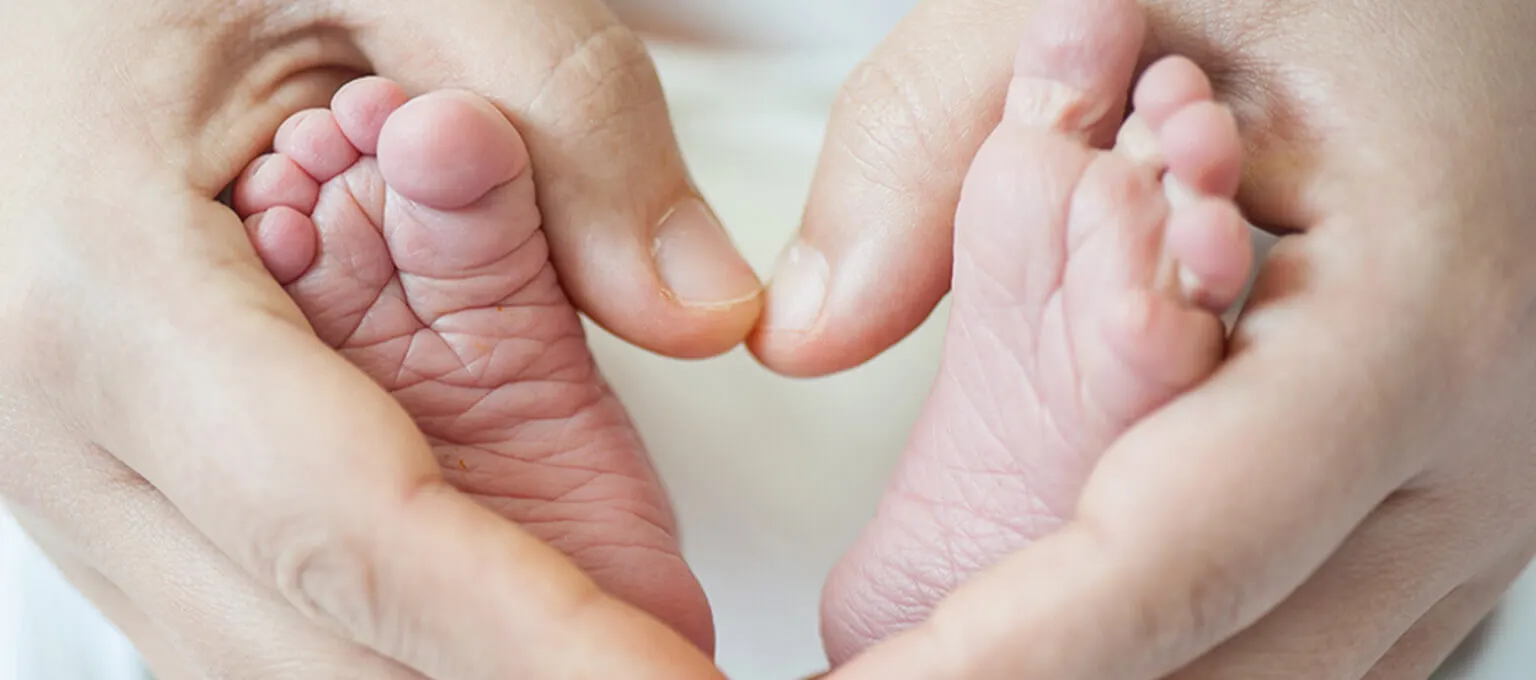 Dłonie ujmujące stópki dziecka ułożone w kształt serca