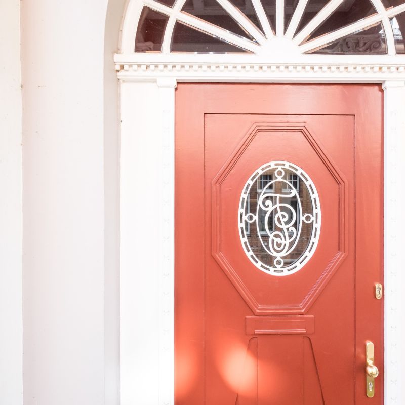Eine rote Haustür mit Altbaucharme und Verzierungen. Die Tür führt in ein Altstadthaus in Lübeck, das von uns mit Liebe zum Detail saniert und aufgearbeitet wurde.