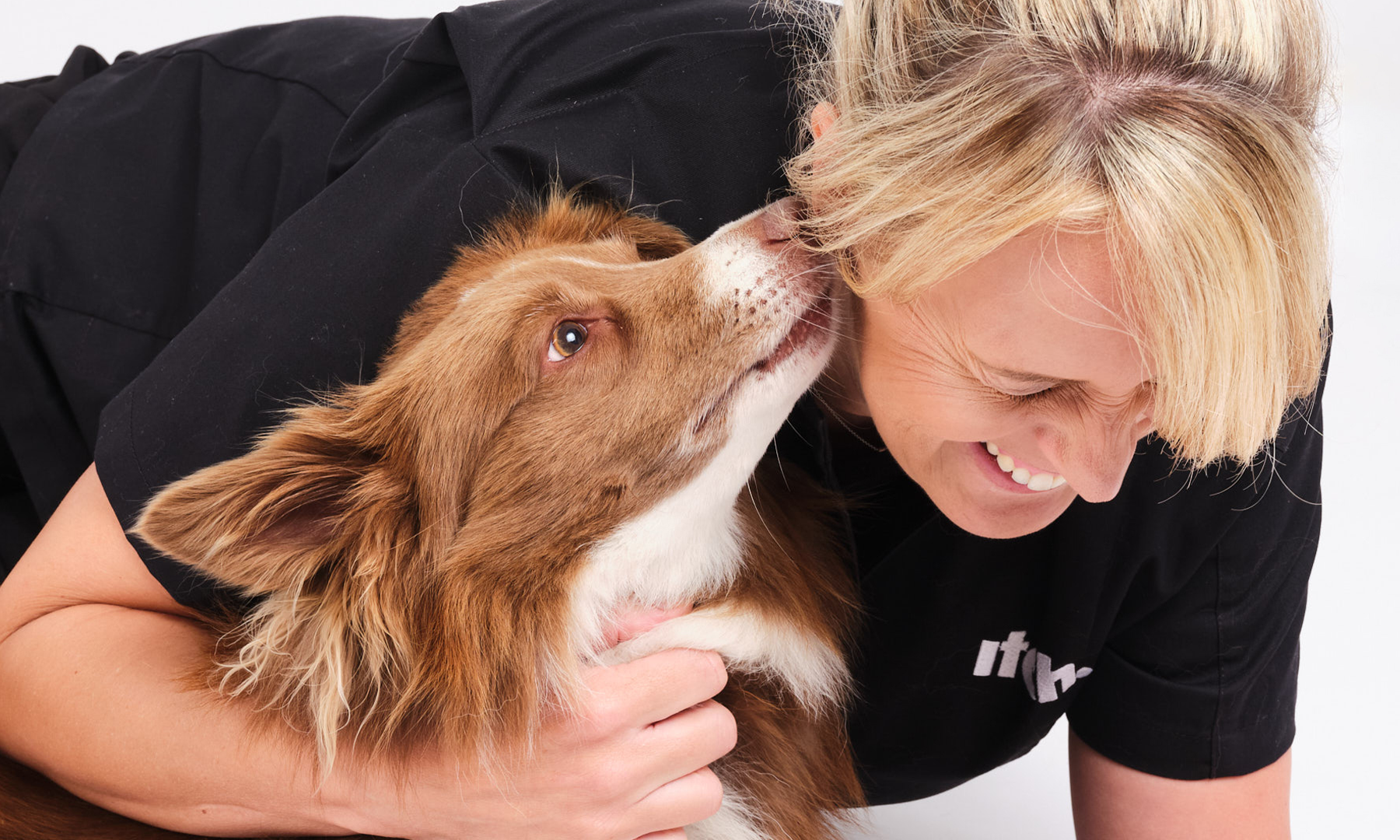 An image of Zoe the vet with Meg the dog. Meg is licking Zoe's ear and Zoe is laughing.