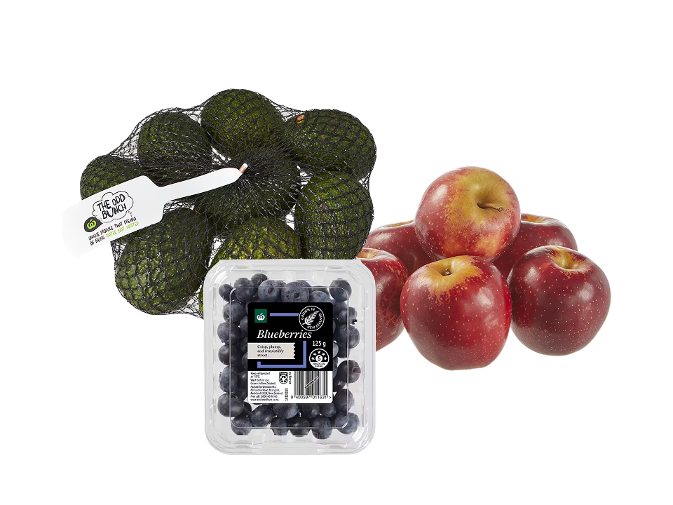 A selection of fresh produce displayed together: a mesh bag of avocados tagged "The Odd Bunch", a plastic clamshell container of fresh blueberries, and a small pile of red apples.