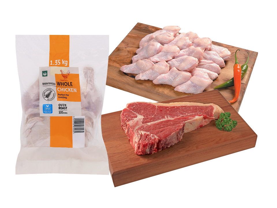 A bagged Woolworths oven roast whole chicken displayed alongside raw chicken wings and a fresh raw T-bone steak on wooden boards.