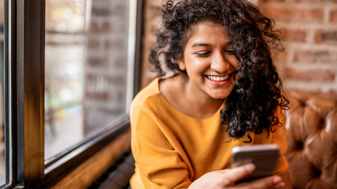 A smiling woman in a yellow shirt using AI image search on her phone