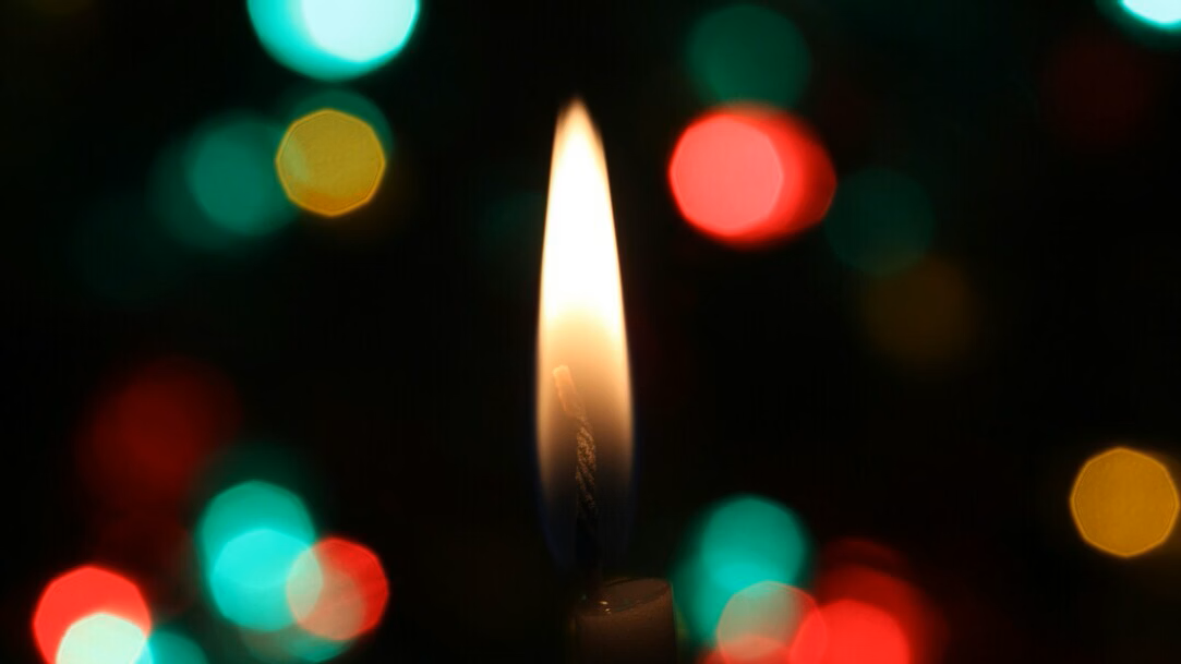 A candle flame against a dark backdrop with red and green and yellow light spots