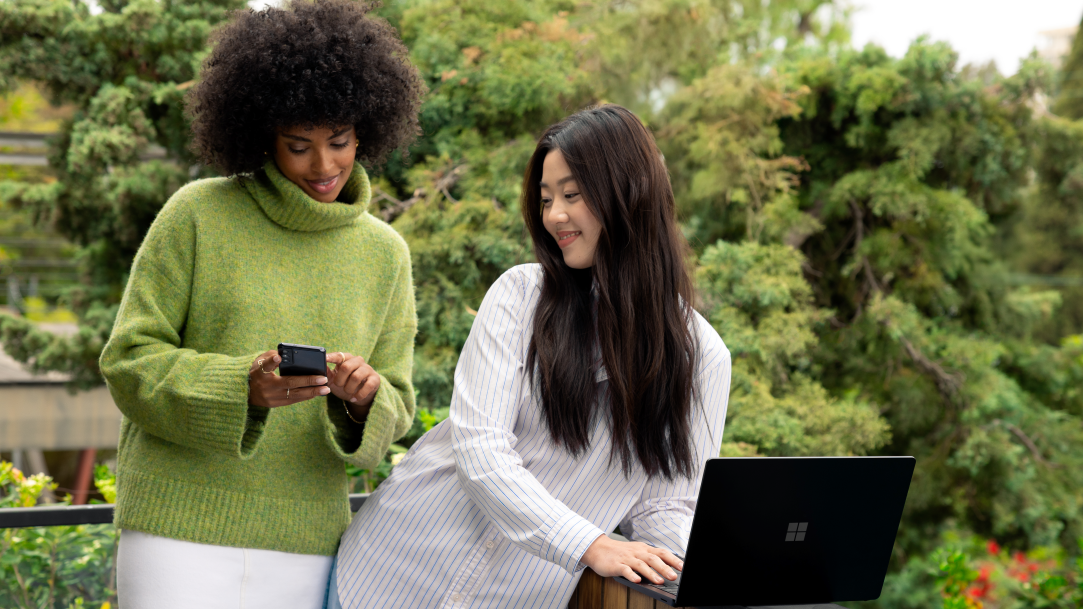 Photography of two adult women outside using a Surface Laptop and a mobile device