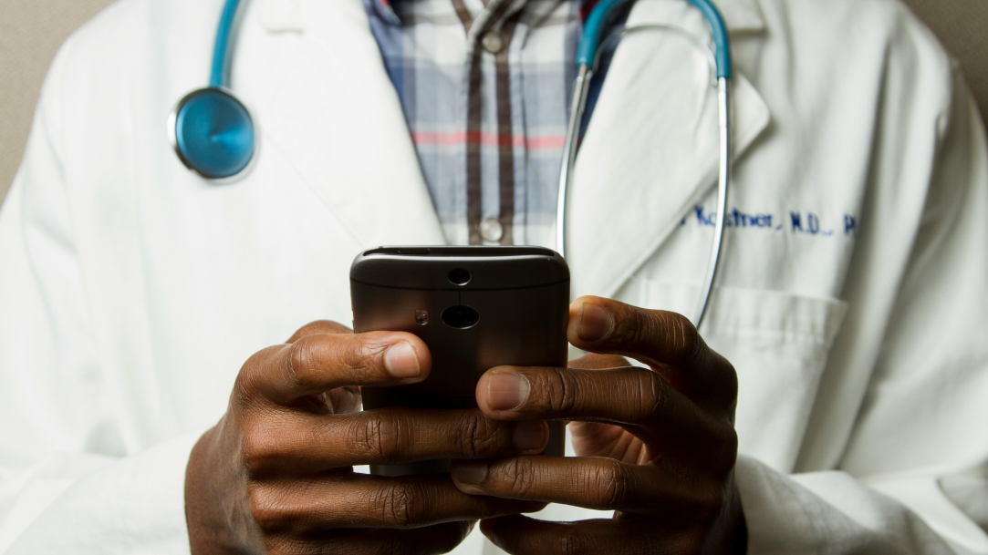 A person wearing a lab coat and stethoscope typing on their mobile phone