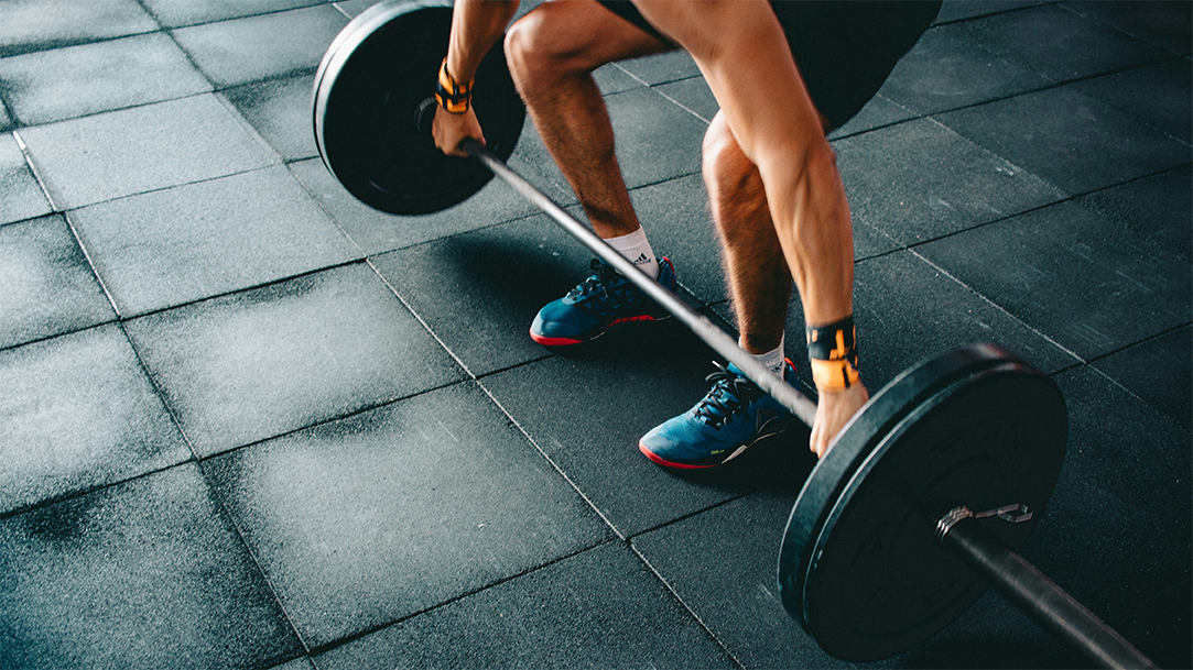 Person lifting a black barbell in an open gym