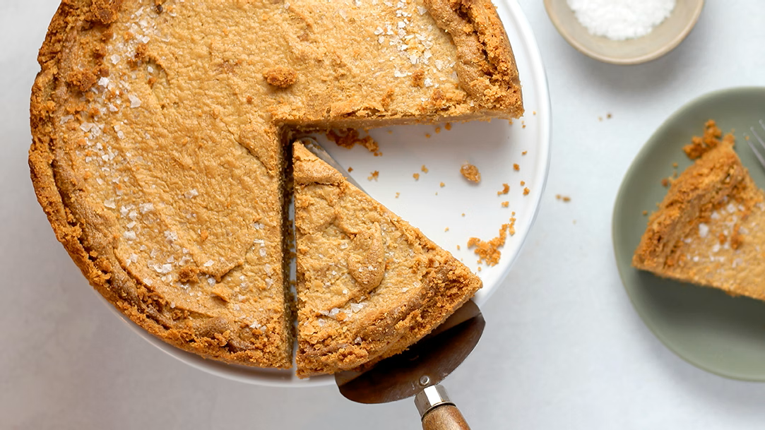 A top-down view of a baked pie on a white stand, with a white plate on the side