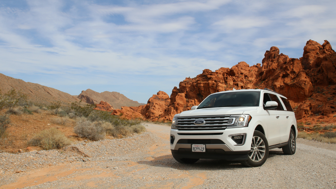 A white SUV parked in the road with red rock cliffs in the background