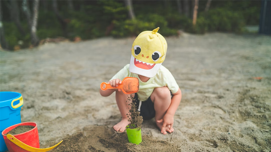 Child in a white shirt and yellow shark hat playing in the sand on a beach
