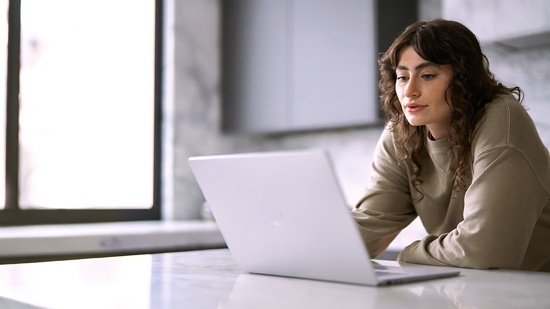 A woman works on her laptop in a kitchen setting