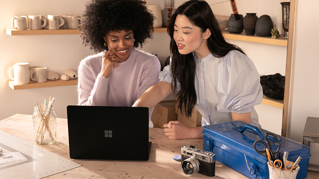 Two artists in a studio referencing a mock-up on a Surface laptop