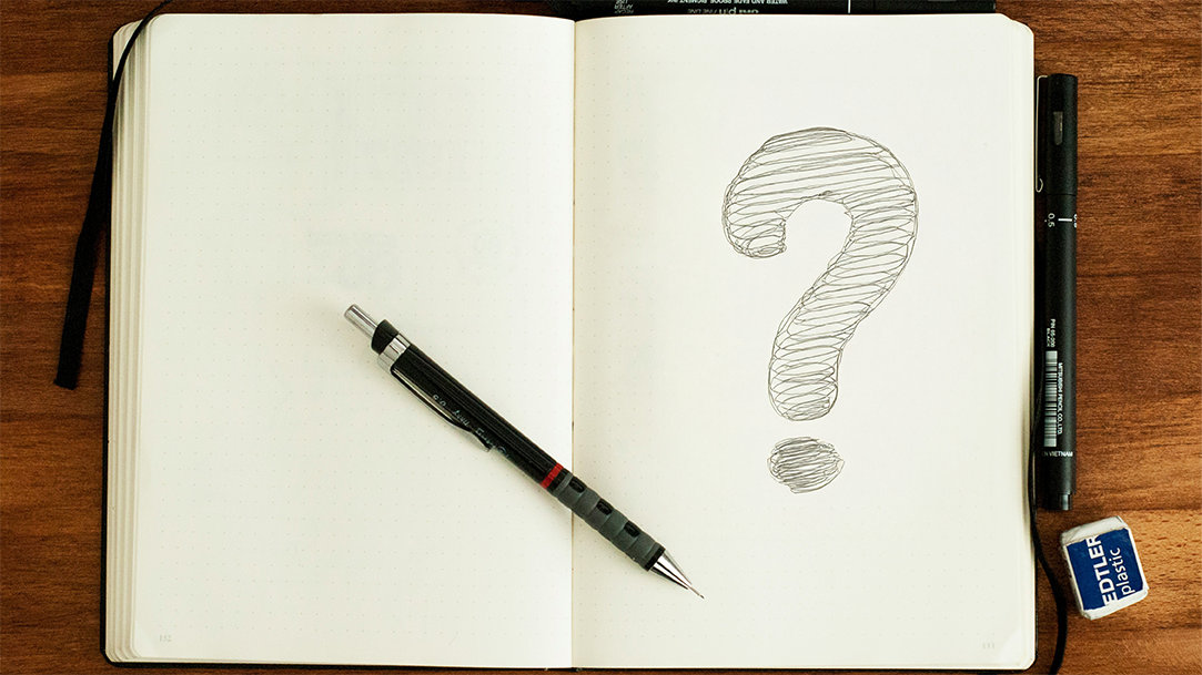 A top-down view of an open blank notebook and pencil w/ a doodle question mark