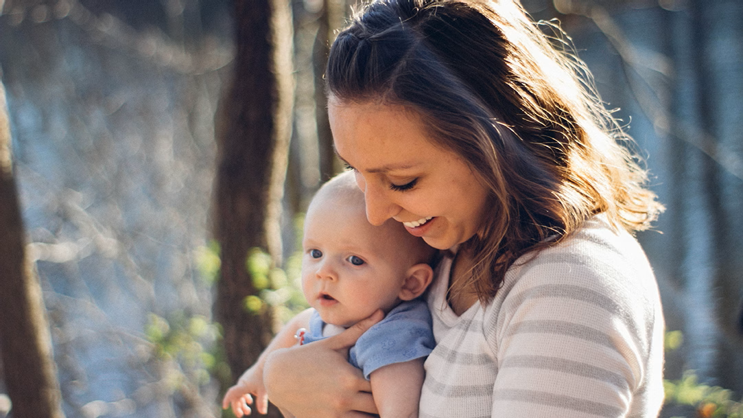 A mom carrying baby outdoors near trees