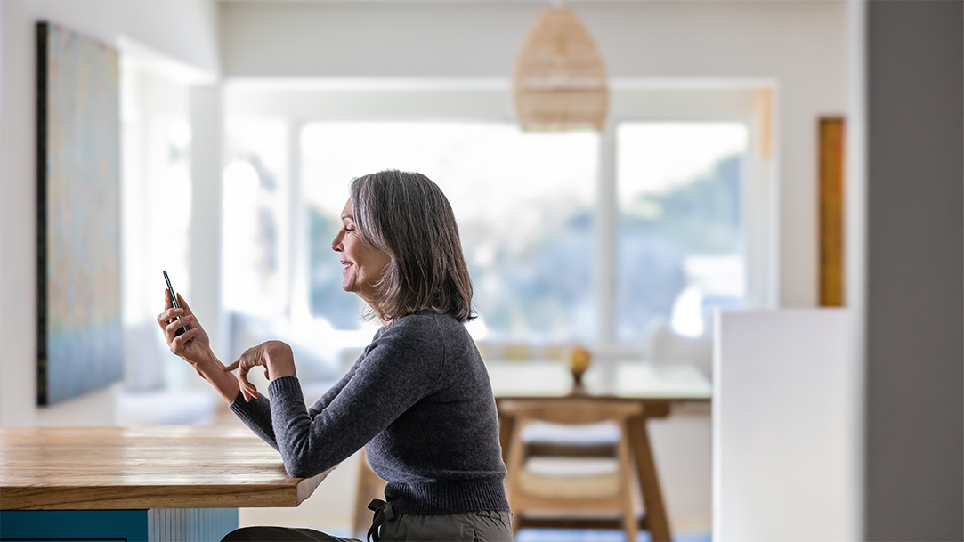 Woman using the Copilot Shopping AI on her mobile device as a price comparison tool in her kitchen