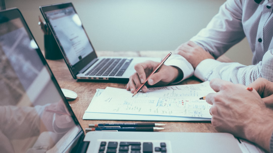Two people completing homework while using their laptops and pen and paper