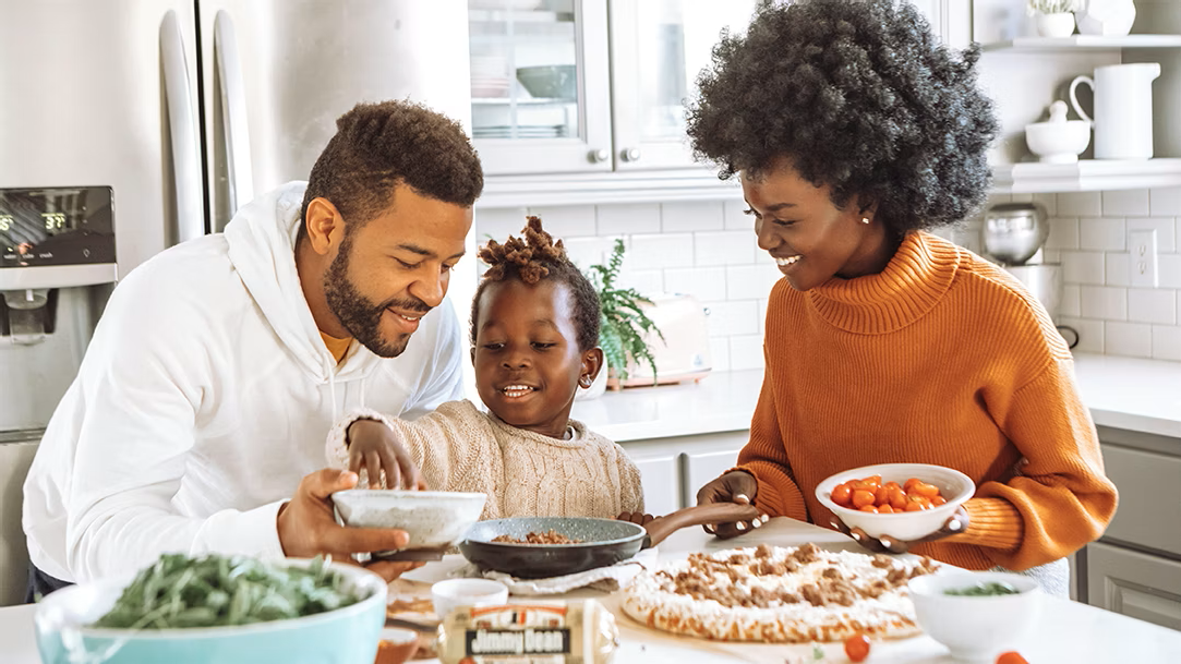 An image of a family together in the kitchen preparing pizza