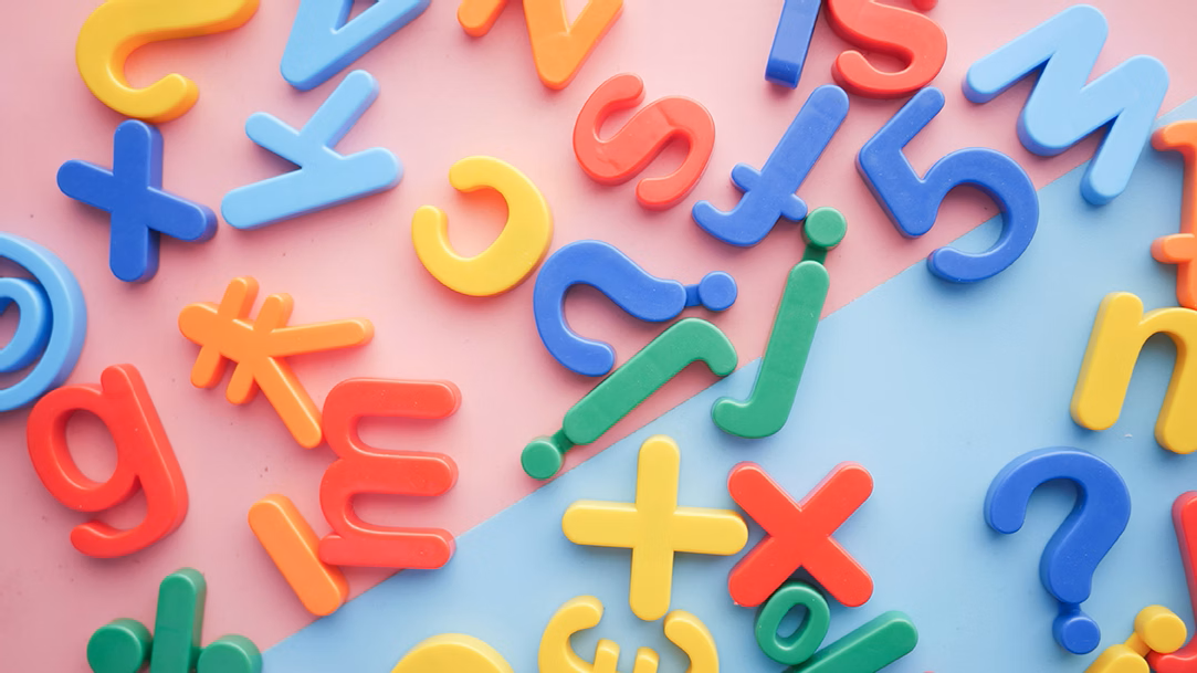 A pile of plastic letters and numbers from different languages on a pink and blue background