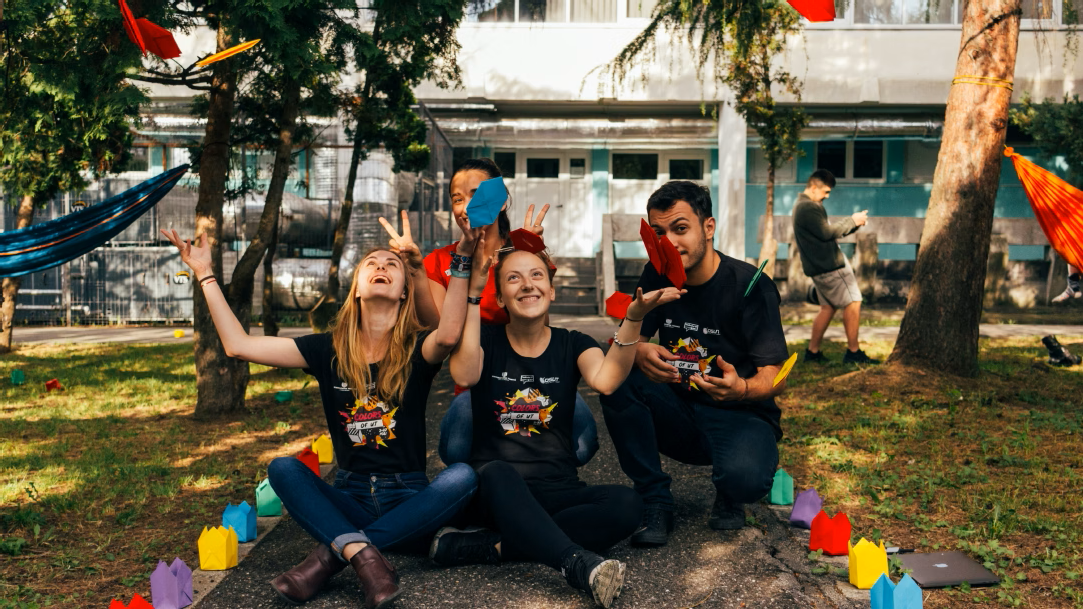Four students sitting on the ground while smiling and throwing colorful paper in the air