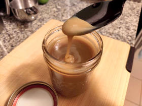 A spoon drizzling caramel sauce from a jar