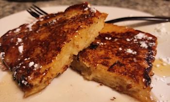 French toast cut in half on a white plate with syrup and powdered sugar