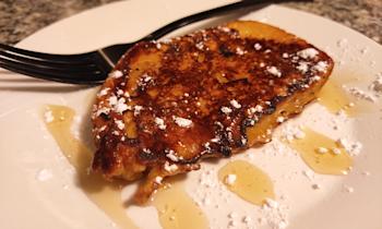 French toast on a white plate with syrup and powdered sugar