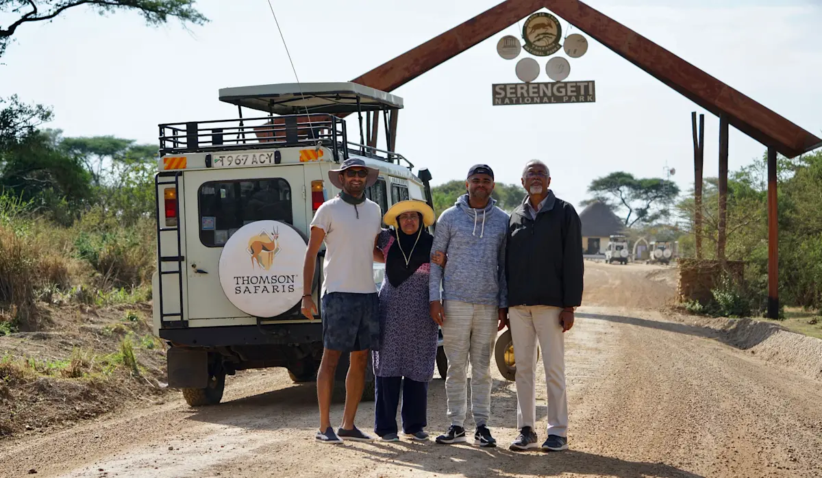 Travelers posing beside a Thomson Safaris vehicle at the Serengeti National Park gate