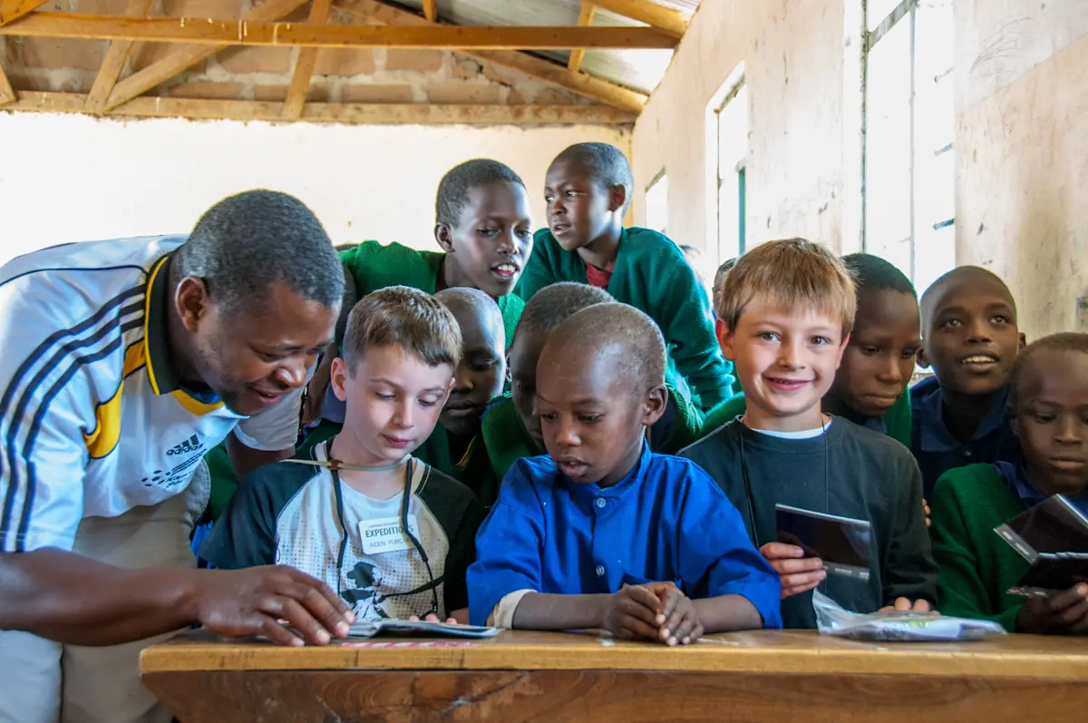 Teacher and young travelers looking at a book with students at a school desk in Tanzania