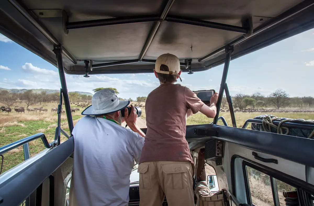 Father and son watching wildlife from the open roof of a safari vehicle in the Serengeti