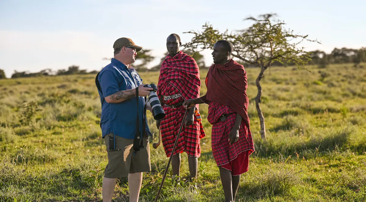 Photographer talking with two Maasai men in red shukas on the Serengeti grasslands
