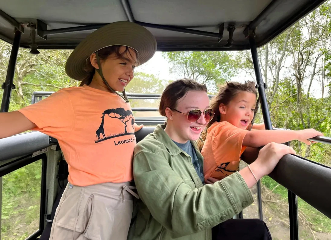 Mother and two daughters smiling and looking out from an open-roof safari vehicle