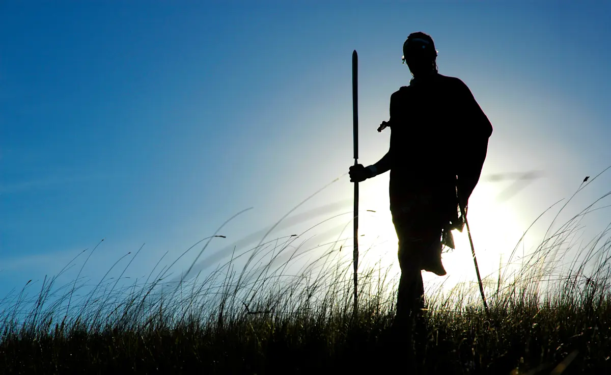 Silhouette of a Maasai man holding a staff against a bright sky in the Ngorongoro Highlands