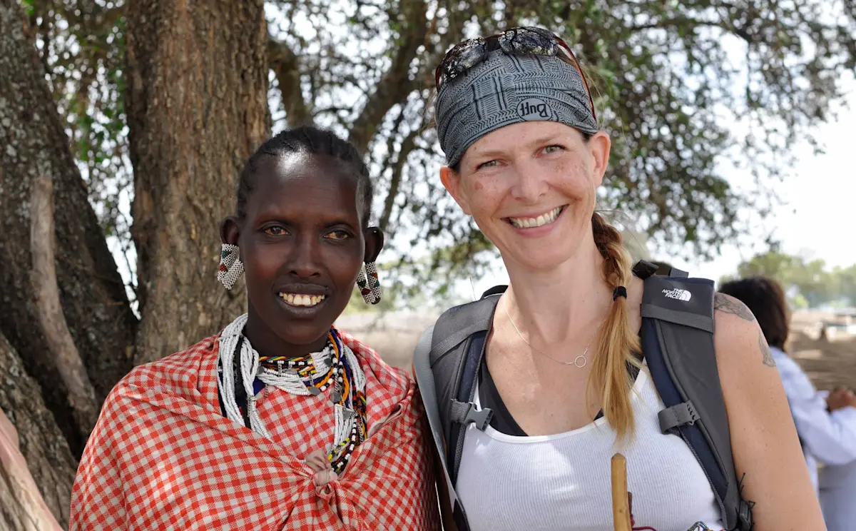Smiling Maasai woman and a guest posing together under a tree in the Eastern Serengeti