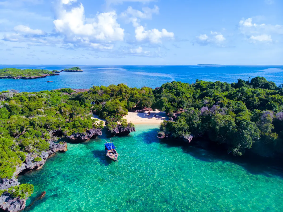 Turquoise lagoon surrounded by green forest and a small boat off the coast of Zanzibar