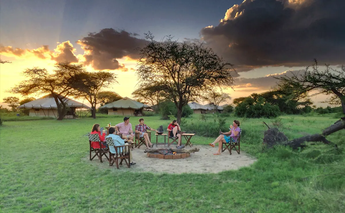 Guests in camp chairs around a fire pit at sundown at Eastern Serengeti Nyumba