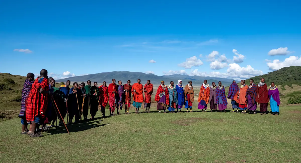 Large group of Maasai men and women in red and purple shukas standing in a line on grassland