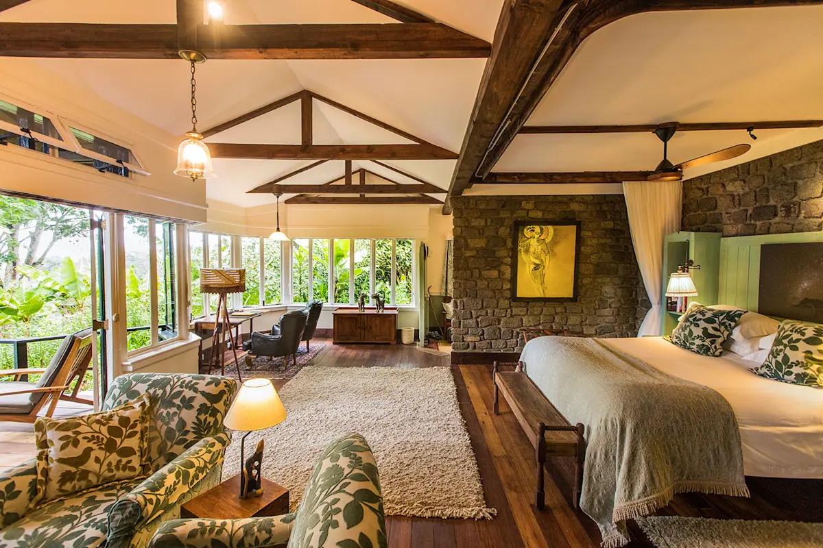 Cottage bedroom with a wood-beamed ceiling, stone wall and sitting area at Gibb's Farm