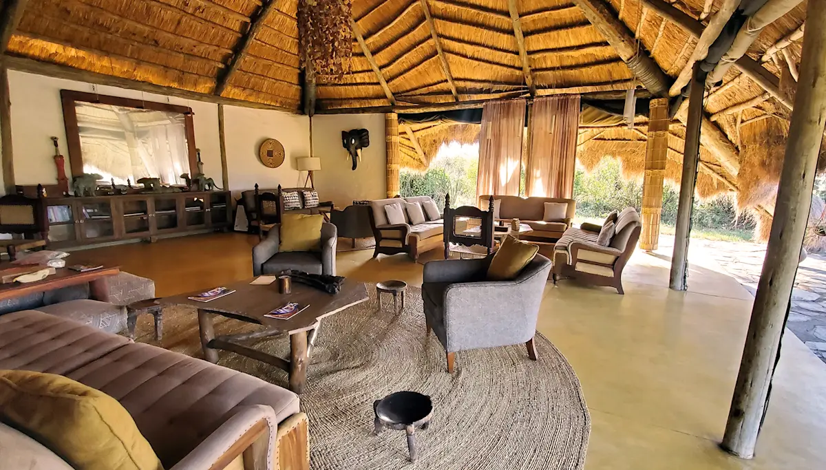 Thatched lounge tent with sofas, armchairs and a rug at Serengeti Nyumba