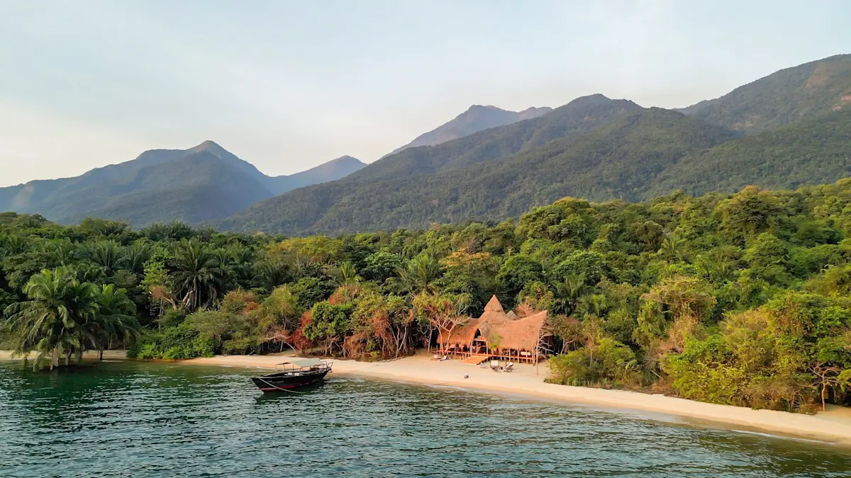 Greystoke Mahale's thatched lodge on a sandy beach below forested mountains, seen from Lake Tanganyika