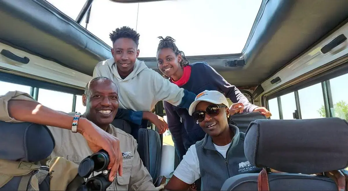Smiling family posing with their guide inside an open-roof safari vehicle