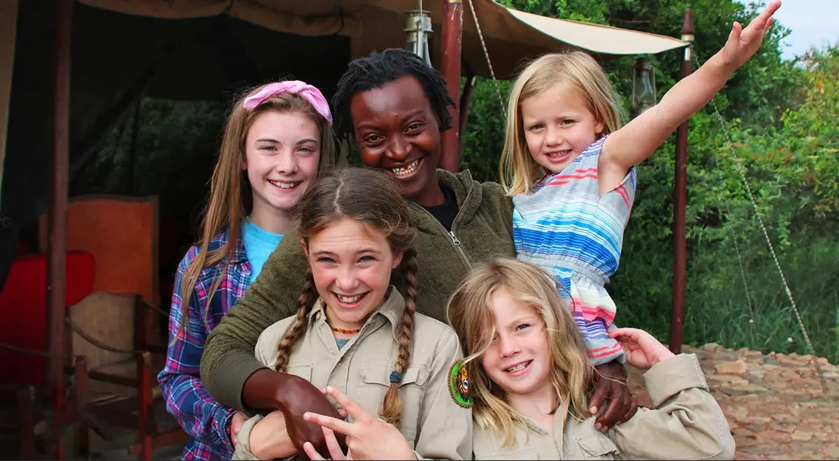 Smiling guide posing with four young girls outside a safari tent