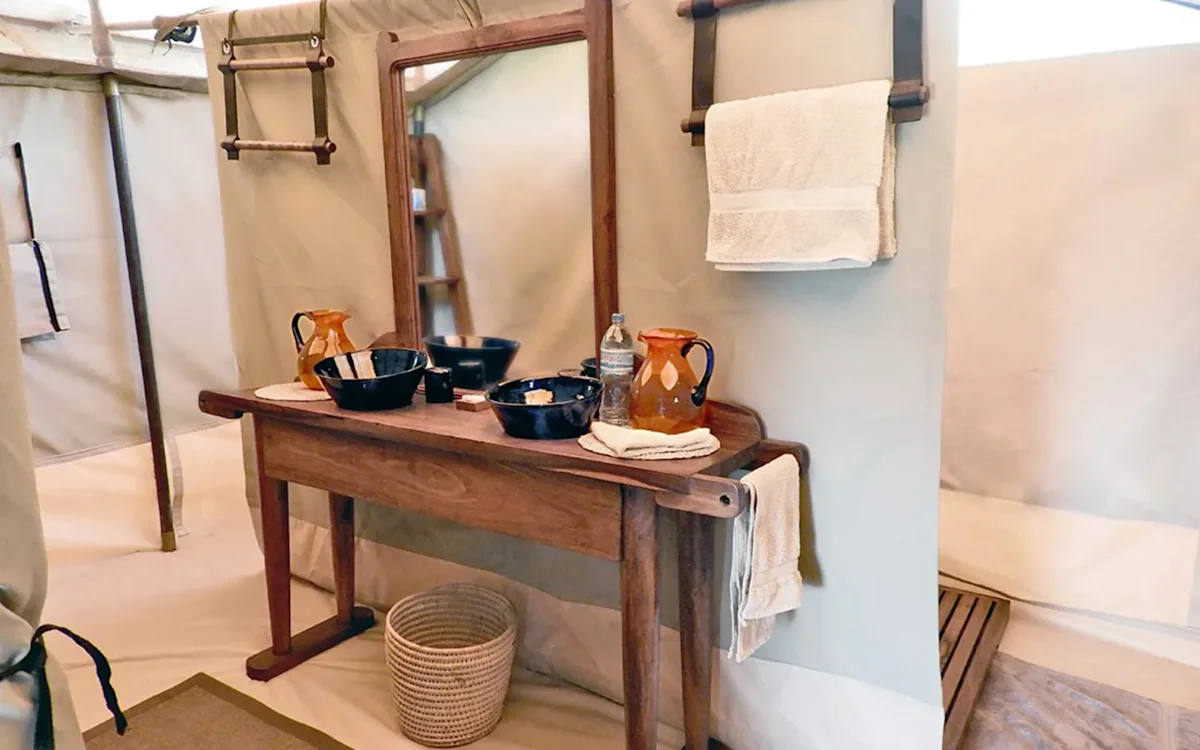 Wooden washstand with water jugs and basins in a tent bathroom at Eastern Serengeti Nyumba