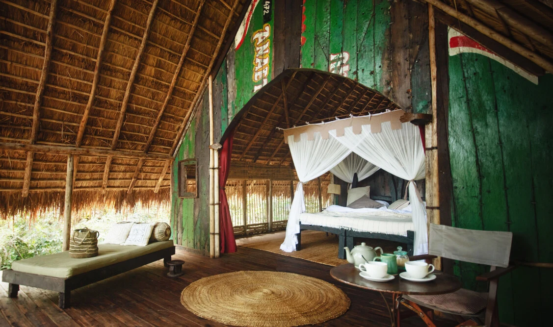 Open-fronted thatched bedroom with a canopy bed and tea set at Greystoke Mahale