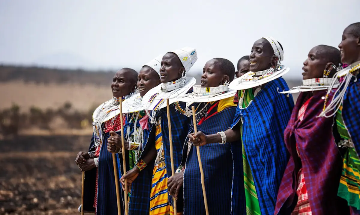 Maasai women in blue wraps and white beaded collars singing together