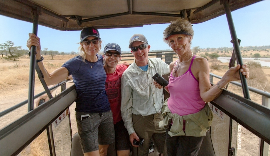 Four smiling guests standing up in an open-roof safari vehicle