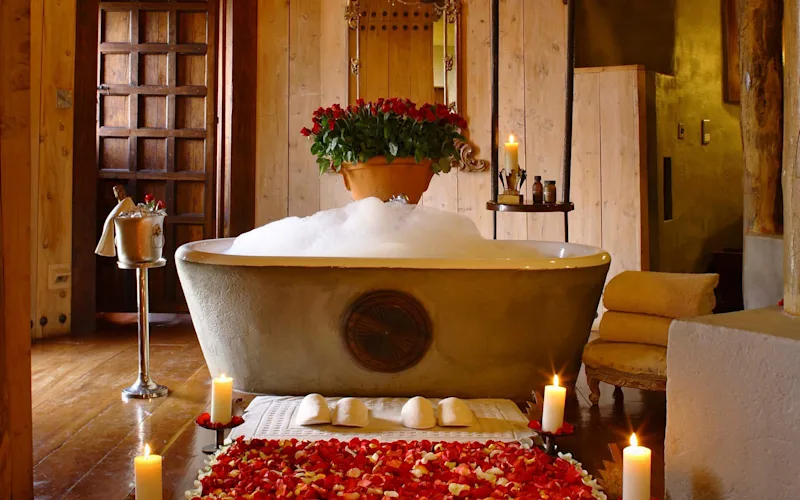 Freestanding bubble bath surrounded by candles and rose petals in a safari lodge suite