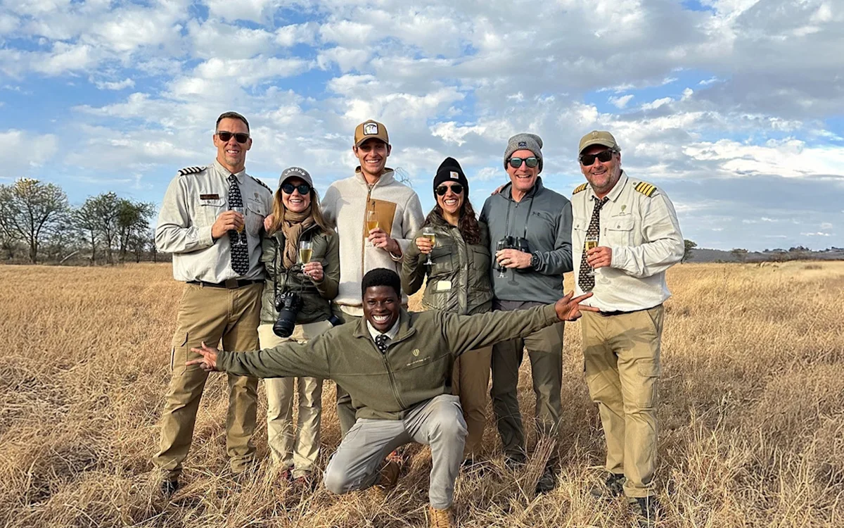 Travelers and balloon pilots posing with drinks on the grassy plains